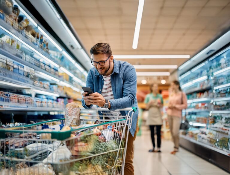 A man browsing his smartphone while shopping in a grocery store aisle.